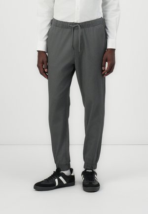 Graue taperte Jogginghosen aus weichem Stoff, mit einem elastischen Bund, verstellbarem Kordelzug und elastischen Bündchen, kombiniert mit schwarzen Sneakers.