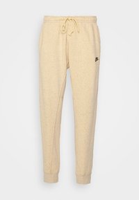 Beiget collegehousut, jotka on valmistettu pilkullisesta kankaasta. Niissä on kiristysnauha vyötäröllä, kapenevat lahkeet ja pieni musta Nike-logo vasemmassa reidessä.