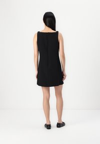 Schwarzes ärmelloses Kleid mit geradem Schnitt, knielang, mit einem Reißverschluss hinten und glattem, strukturiertem Stoff. Schwarze flache Schuhe.
