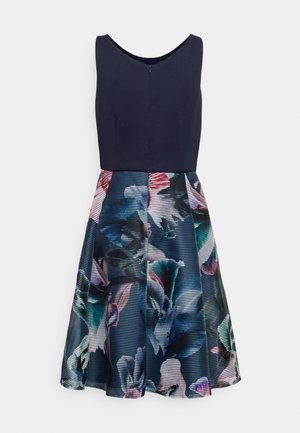 Mouwloze jurk met een effen donkerblauw aansluitend lijfje en een uitlopende rok met een kleurrijk abstract bloemmotief.