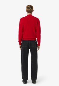 Suéter rojo de punto con un cuello alto, puños y dobladillo acanalados, combinado con jeans de mezclilla negros de corte holgado y zapatillas negras.