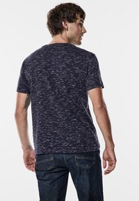 Marinblå kortärmad skjorta med en strukturerad mönster, gjord av mjukt tyg, med rund halsringning och en avslappnad passform, tillsammans med mörka denimjeans.