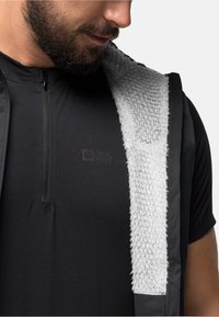 Maglietta nera con zip, dotata di un colletto bianco testurizzato e dettagli grigi, caratterizzata da un design comprimibile e un logo sul petto.
