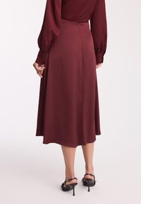 Bordowa satynowa sukienka midi z długimi rękawami, guzikiem na mankietach oraz zamkiem z tyłu. Połączona z czarnymi szpilkami na odkrytej pięcie.