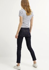Jeans ajustados de mezclilla oscura con un lavado sutil, combinados con una camisa blanca con rayas azules marinas. Zapatillas blancas completan el look casual.