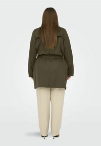 Olivově zelená košilová bunda s páskem a dlouhými rukávy, spojená s volnými béžovými kalhotami. Hladká textura a uvolněný střih.