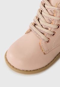 Botte en cuir rose clair avec un bout arrondi, lacets texturés beige et œillets en or rose. Présente des accents festonnés et une semelle en caoutchouc beige.
