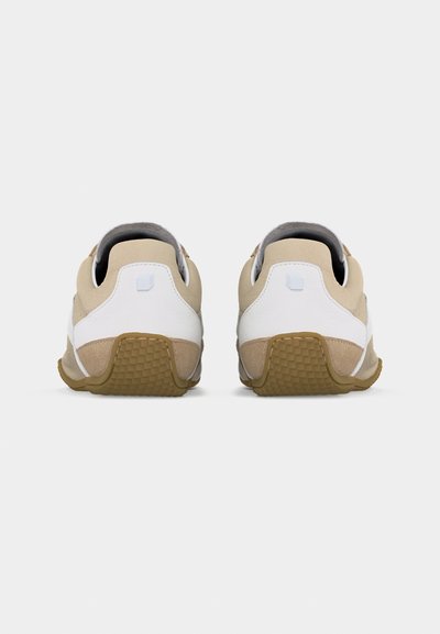 Paire de baskets beige et blanche vues de dos avec des semelles extérieures brunes texturées sur un fond blanc uni.