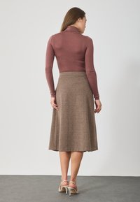 Brąskowa spódnica w kształcie litery A o teksturowanym wykończeniu, zestawiona z dopasowanym, długim rękawem, mauve golfem. Prosty design, bez widocznych wzorów.