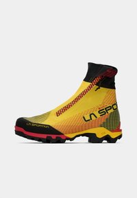 Botas de senderismo impermeables en amarillo y negro, con un collar alto, cierre con cremallera, superficie texturizada, suela agresiva y acentos en rojo en la suela exterior.