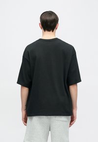 Μαύρο φαρδύ μπλουζάκι, κοντά μανίκια, στρογγυλή λαιμόκοψη. Κατασκευασμένο από βαμβάκι, με ομαλή υφή. Συνδυάζεται με γκρι σορτς, απλό σχέδιο, χωρίς ορατά σχέδια ή λεπτομέρειες.