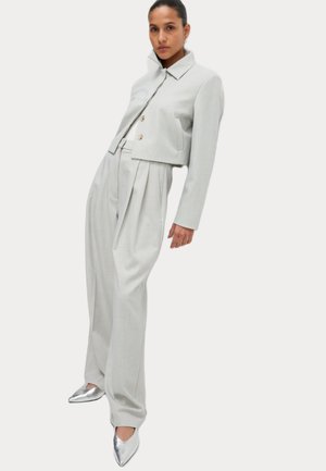 Costume ajusté gris clair avec une veste courte et un pantalon plissé taille haute. Des escarpins argentés à bout pointu complètent l'ensemble.