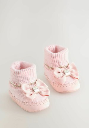 Moufles pour bébé roses avec une cheville en tricot côtelé, de grands nœuds et des coutures décoratives. Matière douce avec une semelle lisse et des détails ornés.