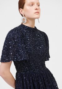 Vestido de lentejuelas en navy con mangas abullonadas y cintura fruncida. Presenta un escote alto y adornos texturizados para un efecto brillante.