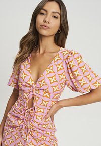Roze en oranje gestreepte jurk met pofmouwen, diepe V-hals en gathered details bij de taille, gemaakt van een zachte, rekbare stof.