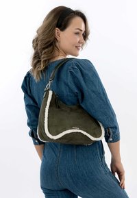 Olive green suede shoulder bag with white faux fur trim, featuring a curved design and a black leather shoulder strap.