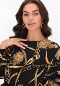 Fekete ruhadarab arany virág- és láncmintával, laza szabással és puffos ujjakkal. Kiegészítők: arany karika fülbevalók és arany gyűrű.
