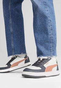 Weiße und marineblaue Sneaker mit einem pinken Akzent, ausgestattet mit einem strukturierten Lederdesign, Schnürverschluss und einer dicken weißen Sohle. Getragen mit fransigen Jeans.