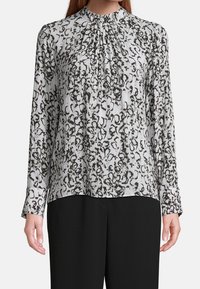 Long-sleeve blouse in light gray with a black abstract pattern, featuring a gathered neckline and cuffs. Soft fabric with a relaxed fit.