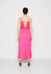 Robe maxi fuchsia sans manches avec un dos décolleté, une taille froncée et de fines bretelles spaghetti. Tissu lisse et brillant avec une silhouette fluide.