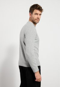 Light gray sweater with a crew neck, ribbed cuffs, and hem. Soft texture, medium thickness, tailored fit, worn with black pants.