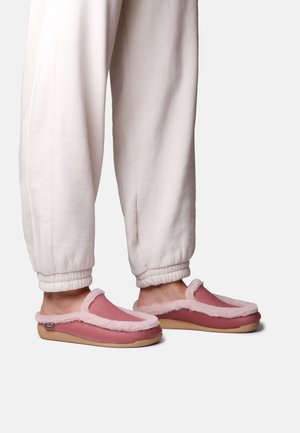 Person wearing light beige sweatpants and pink slip-on slippers with fluffy trim, standing on a white background.