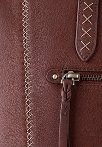 Brown leather bag with textured surface; features beige stitching, braided zipper pull, and metal hardware near zip closure.