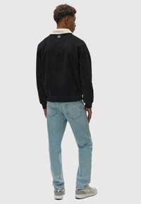 Zwarte corduroy jas met een crèmekleurige nepleren kraag, geribbelde manchetten en een knoopdetail aan de achterkant, gedragen met lichtblauwe jeans en grijze sneakers.