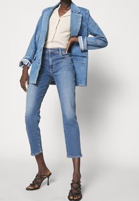 Modrá džínová bunda s ohrnutými rukávy, krémový top, světle modré džíny s detailem na lemu a černé sandály na vysokém podpatku s křížovými popruhy.