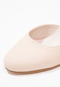 Jasnoróżowe buty wsuwane z teksturowaną powierzchnią, okrągłym noskiem i gładką podszewką wewnętrzną. Minimalistyczny design bez widocznych elementów metalowych.