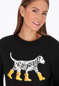 Sudadera negra con un gráfico de un perro dálmata que lleva botas de goma amarillas. El perro tiene manchas negras y blancas, y el diseño está centrado en el pecho.