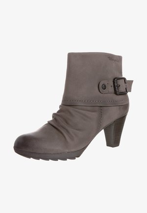 Harmaa nahkasaapas nilkkapituisella, löysällä muotoilulla, pyöristetyllä kärjellä ja koristeellisella soljella sivussa. Varustettu pinotulla korolla ja rakenteellisella pohjalla.