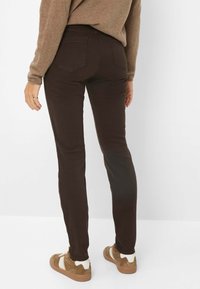 Brune skinny jeans med en glat overflade og baglommer, båret sammen med brune og hvide sneakers. Synlig syning langs siderne.