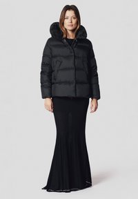 Czarna puchówka z wysokim kołnierzem, poziomym przeszyciem i zapięciem na zamek, zestawiona z długą czarną spódnicą o prążkowanej strukturze i rozkloszowanym dołem.