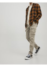 Brun och svart rutigt flanellskjorta över en vit hoodie, i kombination med ljusbeige cargobyxor och svarta sneakers. Avslappnad outfit.