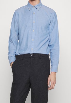 Camicia button-up azzurro chiaro in misto lino, con colletto a punte e maniche lunghe, abbinata a pantaloni sartoriali grigio scuro.