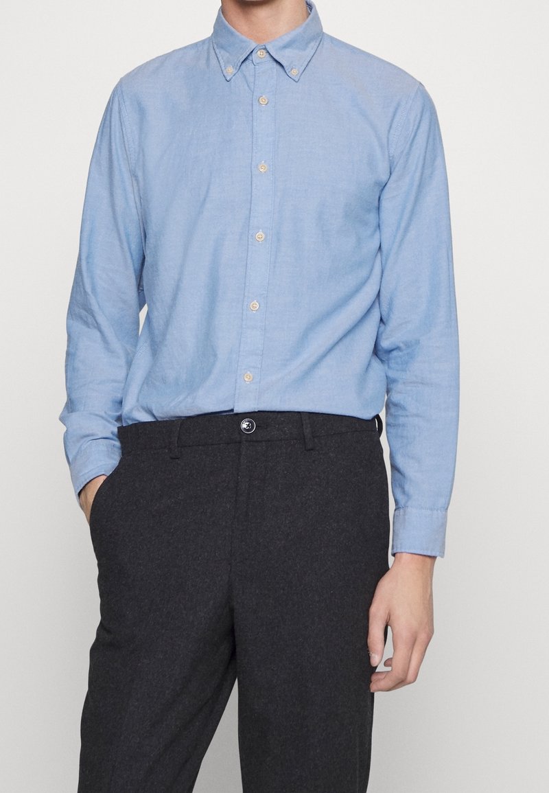 Ljusblå skjorta i linneblandning med spettskärning och lång ärm, i kombination med mörkgrå skräddarsydda byxor.