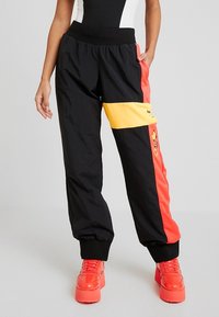 Svarta, lätta joggingsbyxor med livfulla röda och gula sidopaneler. Har elastisk midja och muddar, med kontrasterande logodetalj.