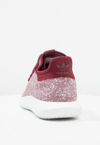 Mörkröda Adidas sneakers med texturerad tygovandel, vit sula och logo på baksidan. Avslappnad design med en dragflik på hälen.