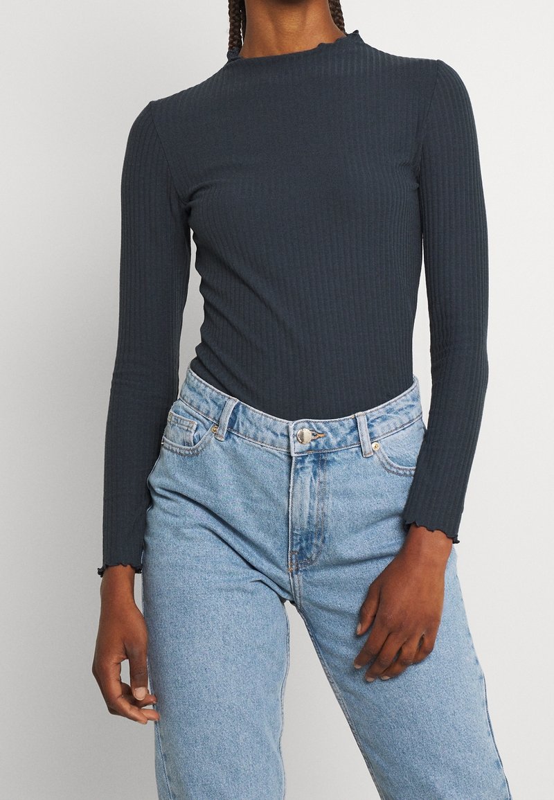 Mörkgrå långärmad ribbad tröja med vågig halsringning, ihop med högmidjade ljusblå denimjeans med klassisk passform och knäppning.