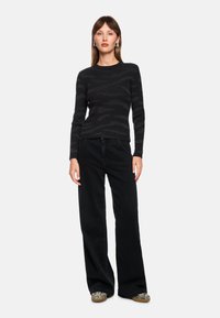 Black knitted sweater with a textured striped pattern, paired with high-waisted black wide-leg pants and patterned slip-on shoes.