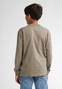 T-shirt a maniche lunghe in cotone verde oliva con scollatura e polsini a coste, vestibilità rilassata, abbinato a jeans in denim blu.