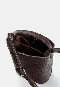 Brun tekstureret lædertaske med åben top, blød inderside og en brun rem med en sølvspænde. Har en indvendig lomme.