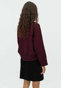Pull en maille bordeaux à coupe décontractée et manches larges, associé à une jupe en velours côtelé noire, vu de dos.