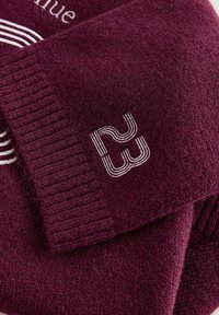 Burgundy villahuivi ja hattu, joissa on ribbitekstuuri, valkoiset brodeeratut kuvastot ja logo hupussa. Pehmeä, lämmin materiaali.