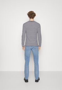 Långärmad randig skjorta i marinblått och vitt, i kombination med ljusblå jeans. Klädseln har en åtsittande silhuett och minimal hårdvara.