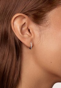 Orecchino a cerchio in argento con un design liscio e arrotondato. Superficie riflettente, dimensioni medie, si adatta perfettamente al lobo dell'orecchio su una pelle chiara.
