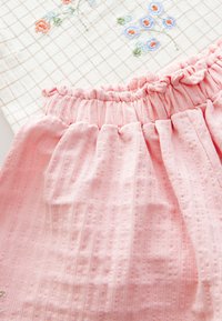 Roosa tekstuuriga kangas kogutud vöökohaga, kõrval beež ruudulise mustriga kangas sinise ja oranži lilleõisete tikandiga.