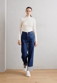 Top alb cu mâneci lungi, cu un design înfășurat, asortat cu blugi albaștri cu talie înaltă și adidași albi. Texturi fine și croială lejeră.