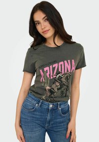 Camiseta gris con gráfico rosa de "ARIZONA" y diseño de rodeo. Mangas cortas, cuello redondo. Combinada con jeans de mezclilla azules.